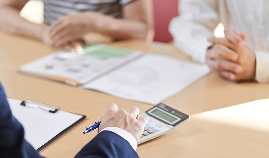 businessman uses a calculator on a table, in a meeting with a couple