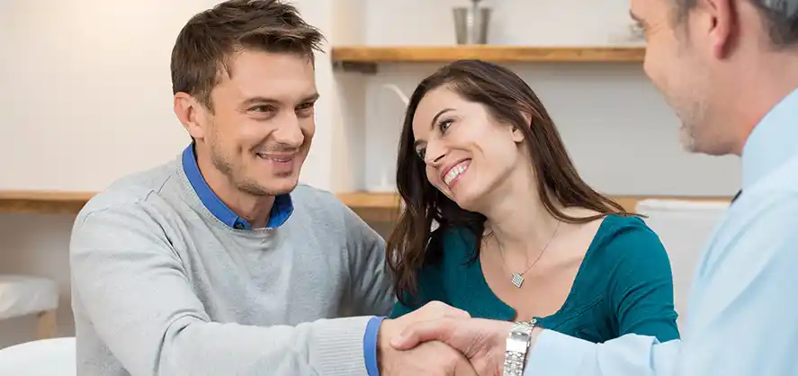 couple smiles as they shake the hand of home buyer/realtor