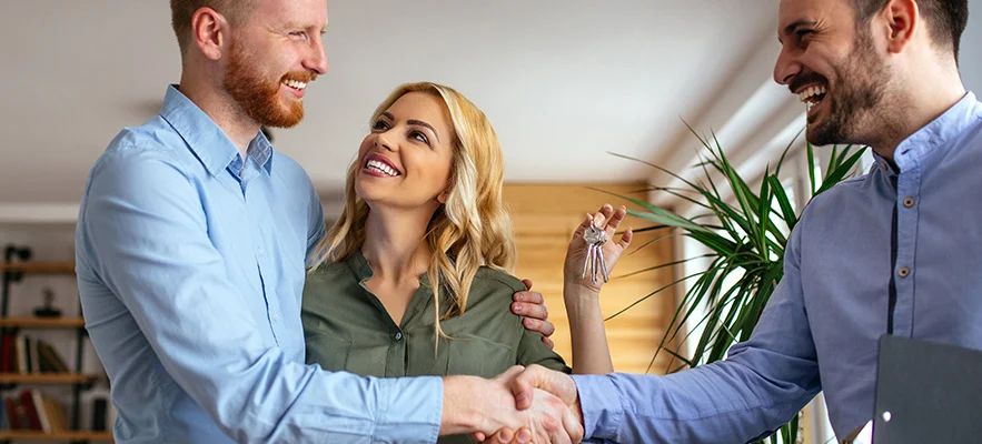 couple shakes the hand of a businessman, holding keys to new home